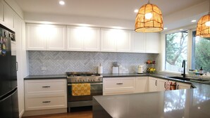 A modern kitchen with white cabinets, a herringbone backsplash, a central island, and pendant lighting.