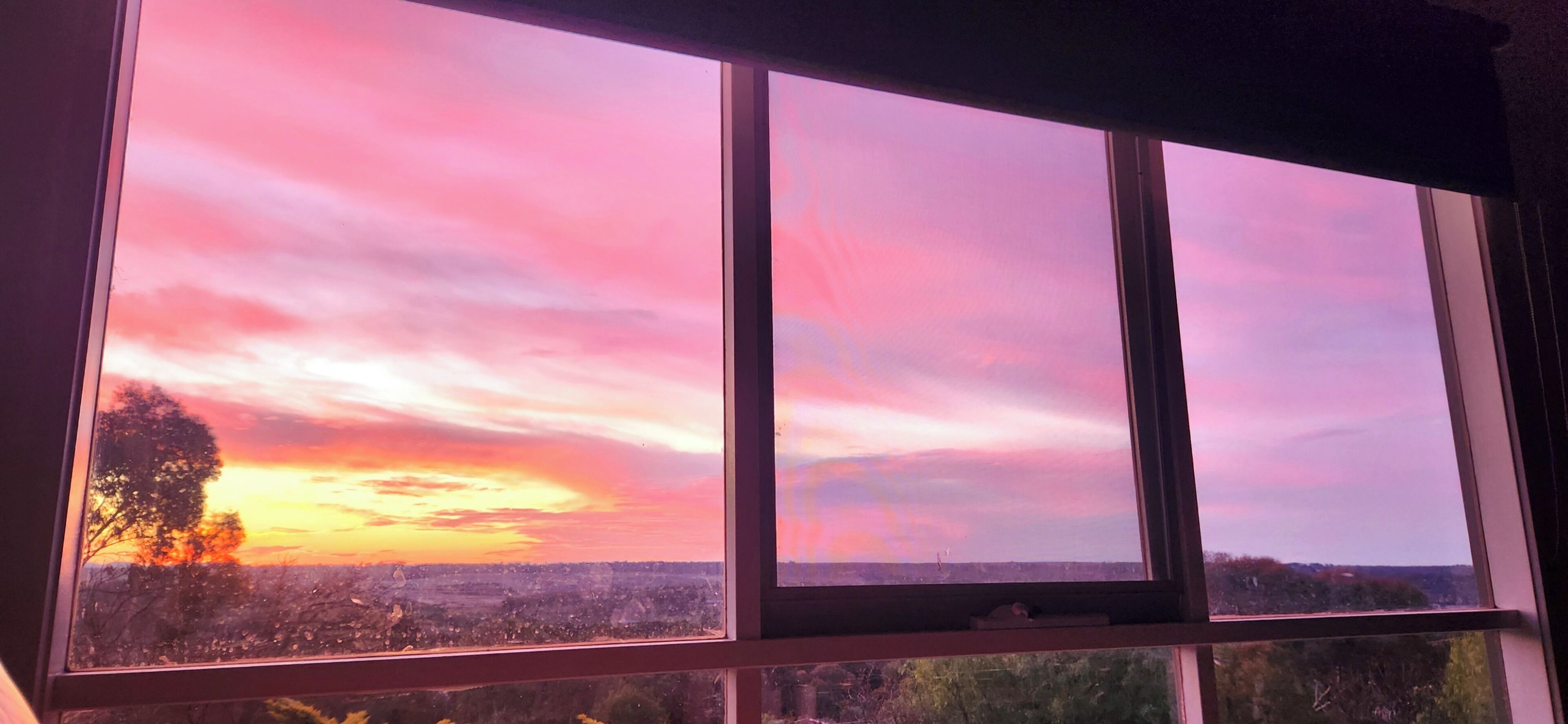 Ein Fenster mit Blick auf einen Sonnenuntergang über einer Stadtlandschaft.