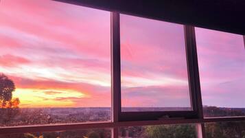 Ein Fenster mit Blick auf einen Sonnenuntergang über einer Stadtlandschaft.
