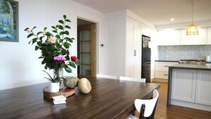 A modern kitchen with white cabinets, a wooden dining table, and a hanging pendant light.
