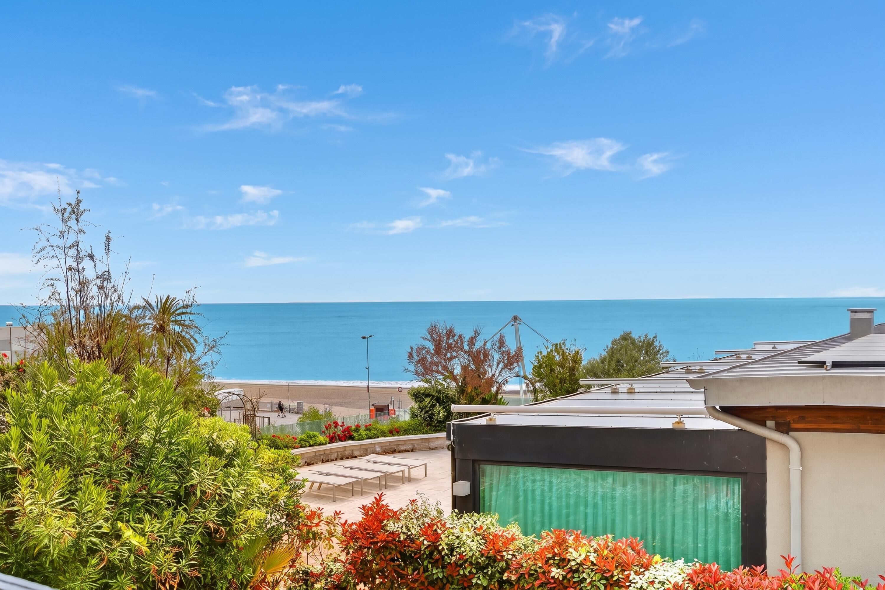 A coastal property with a view of the sea, a garden with various plants, and a building with a green awning.