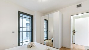 Ein modernes Hotelzimmer mit einem großen Bett, einem Fenster, einem Kleiderschrank und einer Tür zum Badezimmer.
