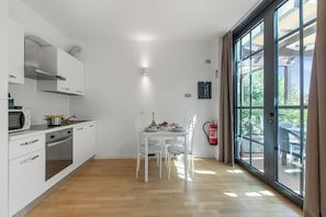 A modern kitchen with white cabinets, a built-in oven, and a dining area with a table and chairs.