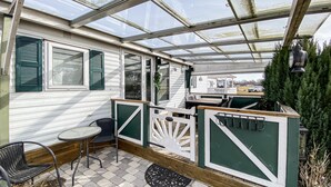 Un patio cubierto con una mesa y sillas, una terraza de madera y una estructura tipo invernadero.