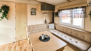 Interior acogedor de una caravana con una mesa de madera, asientos de banco acolchados, una lámpara colgante y una ventana con cortinas.