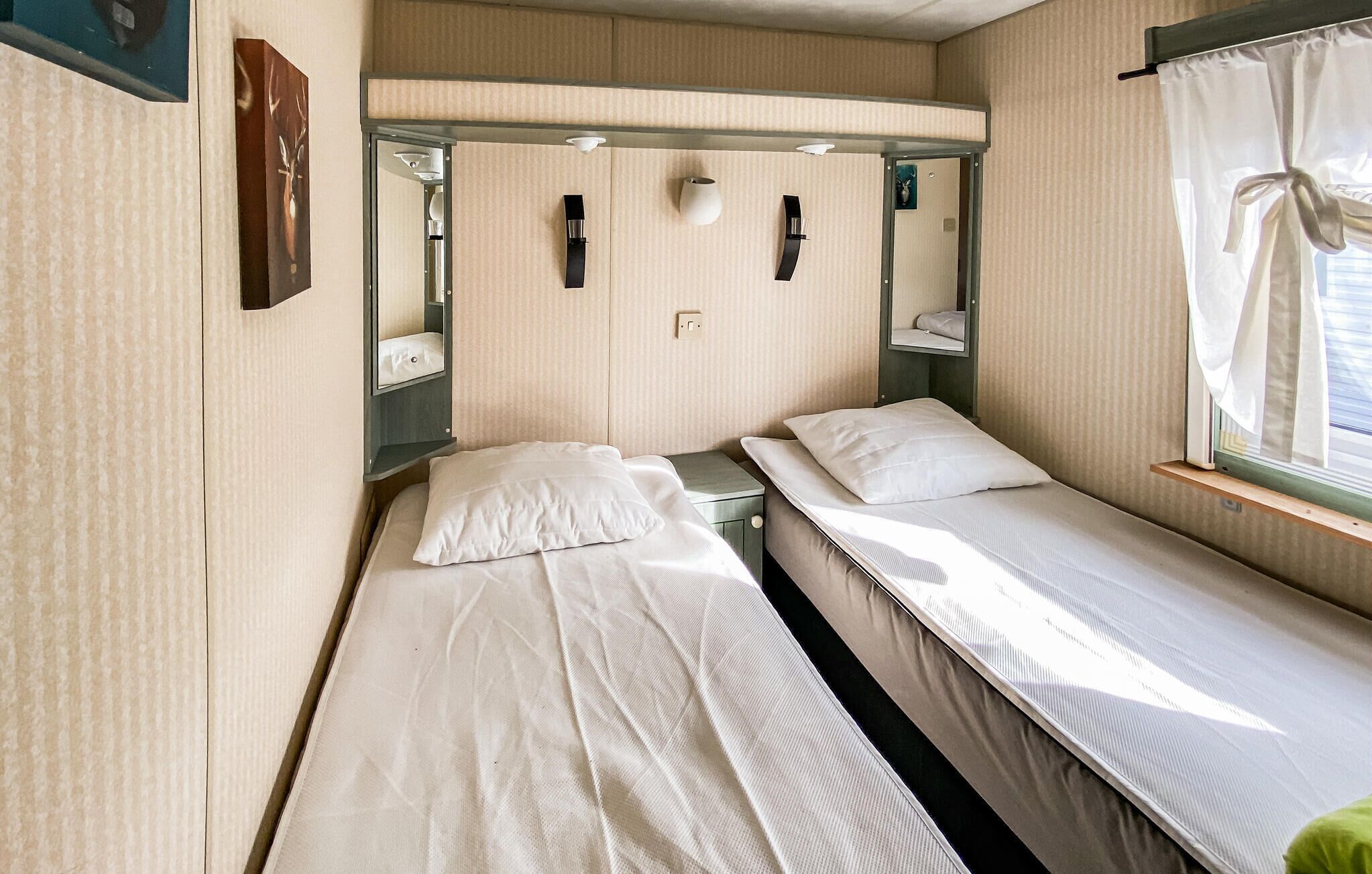 Een compacte, eenkamerhut met twee bedden, een klein raam met gordijnen en een spiegel boven de bedden.