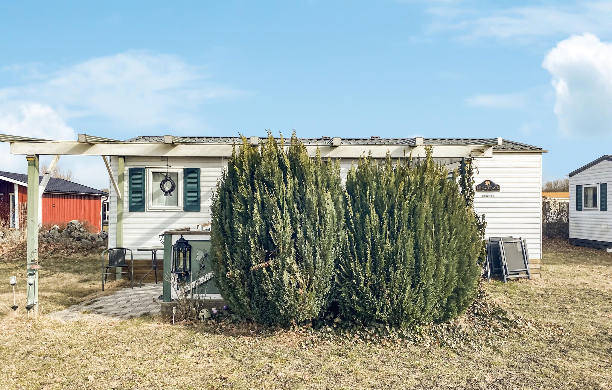 Valkoinen siirtokoti, jossa on kuisti, pieni puutarha ja kyltti, jossa lukee: »LE COTTAGE».