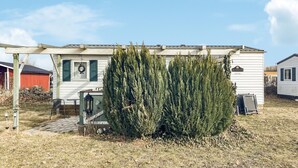 Una casa móvil blanca con un porche, un pequeño jardín y un letrero que dice 'LE COTTAGE'.