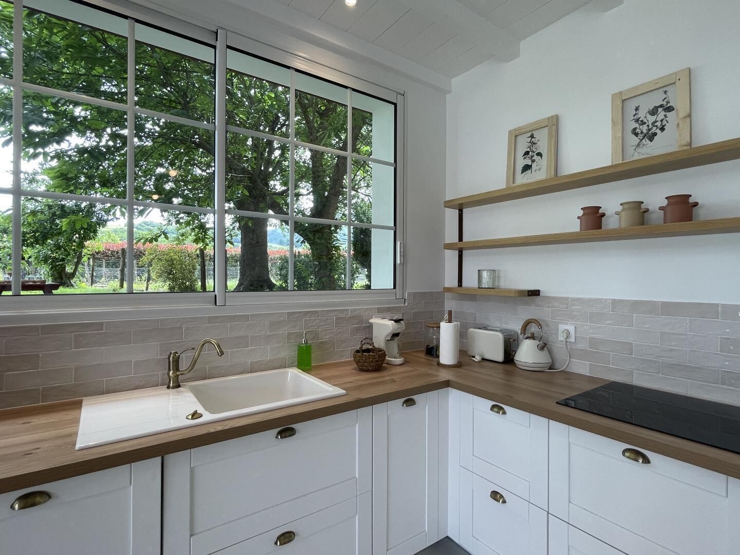 A modern kitchen with a large window, white cabinets, and a wooden countertop.