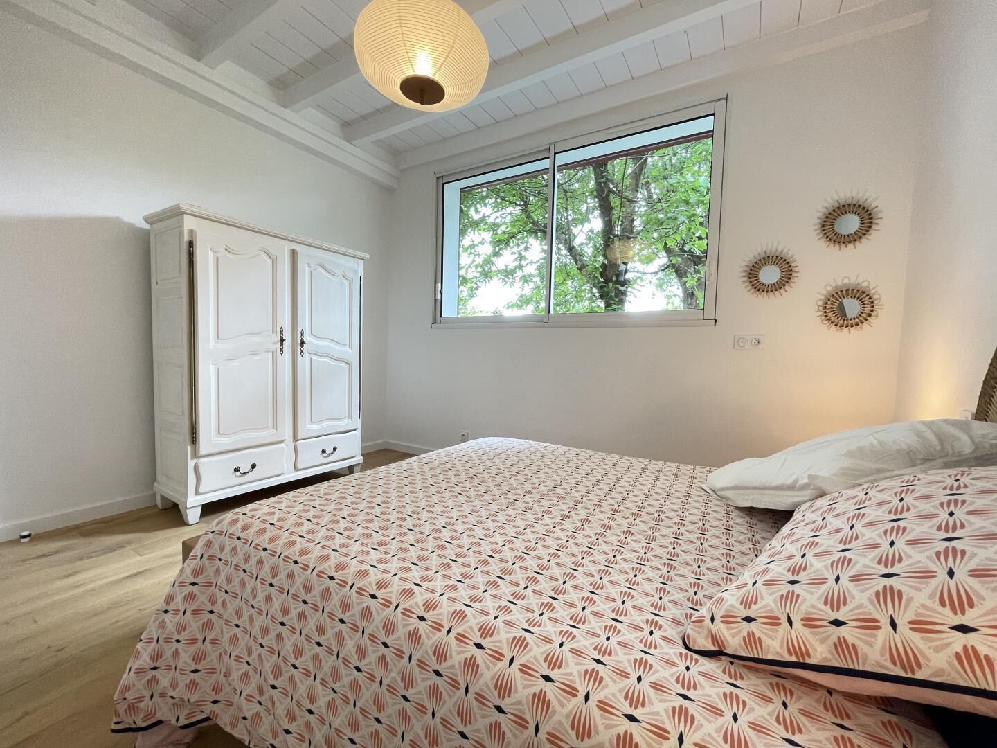Une chambre à coucher comprenant un lit, une armoire, une fenêtre donnant sur des arbres et des éléments de décoration murale.