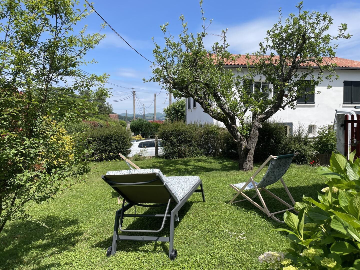 Un espacio al aire libre con césped, dos sillones de lounge y un edificio blanco al fondo.