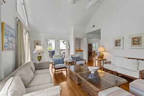 Uma sala de estar ampla com um sofá, cadeiras, uma mesa de centro de vidro e um espaço de jantar com mesa e cadeiras.
