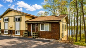 A two-story lodge with a front porch, a small deck, and a view of a lake. - Serenity Now 4BR Lakefront Cabin + Trail Access - Sleeps 12 (Hurley)