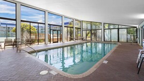 An indoor swimming pool with clear glass walls, a brick floor, and metal pool ladders. - Beachfront Condo | Pool Views, Private Balcony, Walk to Beach, Sleeps 6 | BEACHBALL PROPERTIES (Orange Beach)
