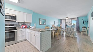 A kitchen with white cabinets, a microwave, an oven, and a dining area with chairs and a table. - Beachfront Condo | Pool Views, Private Balcony, Walk to Beach, Sleeps 6 | BEACHBALL PROPERTIES (Orange Beach)