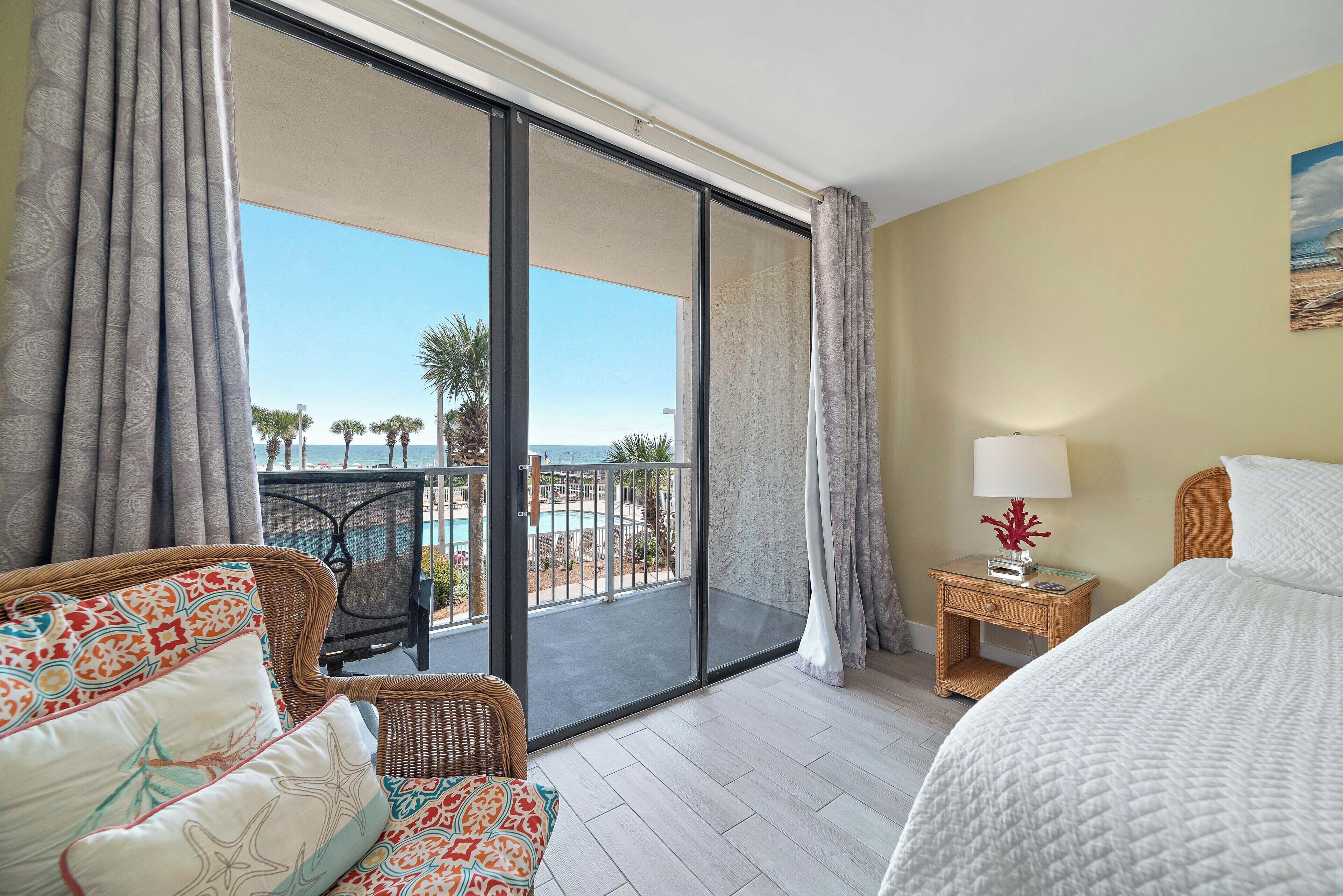 A hotel room with a balcony, a bed, a chair, a nightstand, and a view of the ocean.