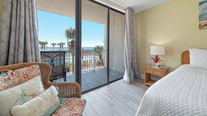 A hotel room with a balcony, a bed, a chair, a nightstand, and a view of the ocean. - Beachfront Condo | Pool Views, Private Balcony, Walk to Beach, Sleeps 6 | BEACHBALL PROPERTIES (Orange Beach)