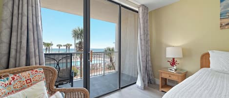 A hotel room with a balcony, a bed, a chair, a nightstand, and a view of the ocean.