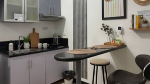 Eine Küche mit schwarzer Arbeitsplatte, weißen Schränken, einer Kaffeemaschine und einer kleinen Essecke mit Hockstühlen.