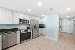 A modern kitchen with white cabinets, stainless steel appliances, and a light blue accent wall. - Beachfront • Lazy River • Sleeps 8 • C305 (Fort Walton Beach)