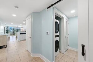 A modern kitchen with white cabinets and a central island, a laundry area with a washing machine, and a dining area with a table and chairs. - Beachfront • Lazy River • Sleeps 8 • C305 (Fort Walton Beach)