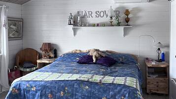 A bedroom with a bed, a shelf with decorative items, a chair, and a desk with a lamp.