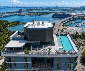 Ein modernes Hotel mit Dachpool, einer großen Rundstruktur und Blick auf den Yachthafen sowie die Stadtlandschaft.