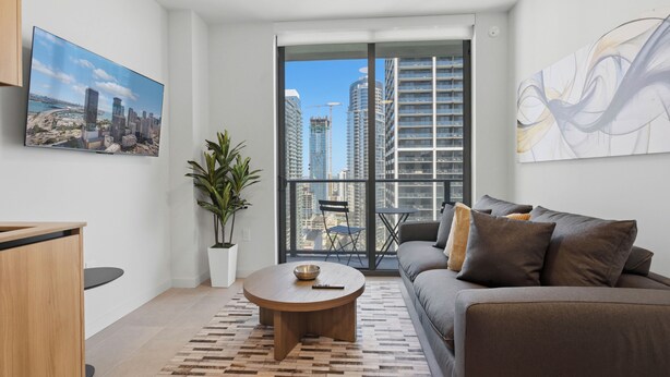 A modern living room with a large window, a sofa, a coffee table, a TV, and a potted plant. - 501 First Luxury Ocean View from Balcony Rooftop Pool & GYM 3511 (Miami)