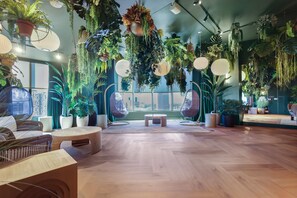 Ein Zimmer mit Holzboden, Korbmöbeln, hängenden Pflanzen und großen Fenstern.