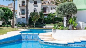A swimming pool with a geometric tile pattern, surrounded by a white building with balconies and a green roof. - SR Las Cancelas 3BDR townhouse in Marbella Centre (Marbella)