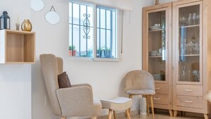 A living room with two armchairs, a small table, a cabinet with glass doors, a window with a view of the outside, and wall-mounted decor. - SR Las Cancelas 3BDR townhouse in Marbella Centre (Marbella)