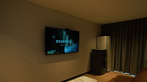 A modern living room with a flat-screen TV mounted on the wall, a marble coffee table, a brown sofa, and a refrigerator. - Ramada Encore ASAN (Asan)