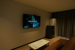 Un salon moderne avec un téléviseur à écran plat fixé au mur, une table basse en marbre, un canapé marron et un réfrigérateur.