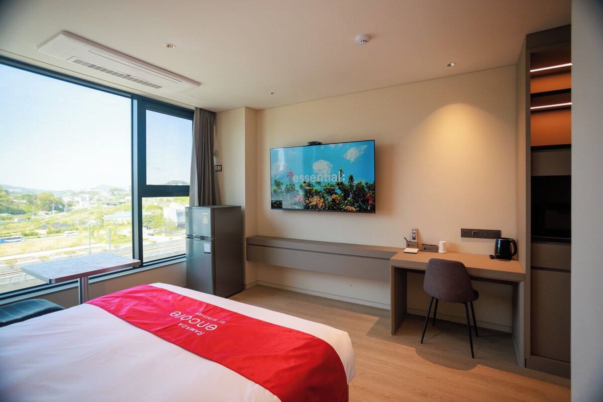 A hotel room with a bed, a desk, a chair, a television, and a view of the city.