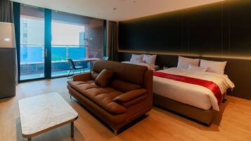 A hotel room with a bed, a sofa, a small table, and a view of the city through large windows.