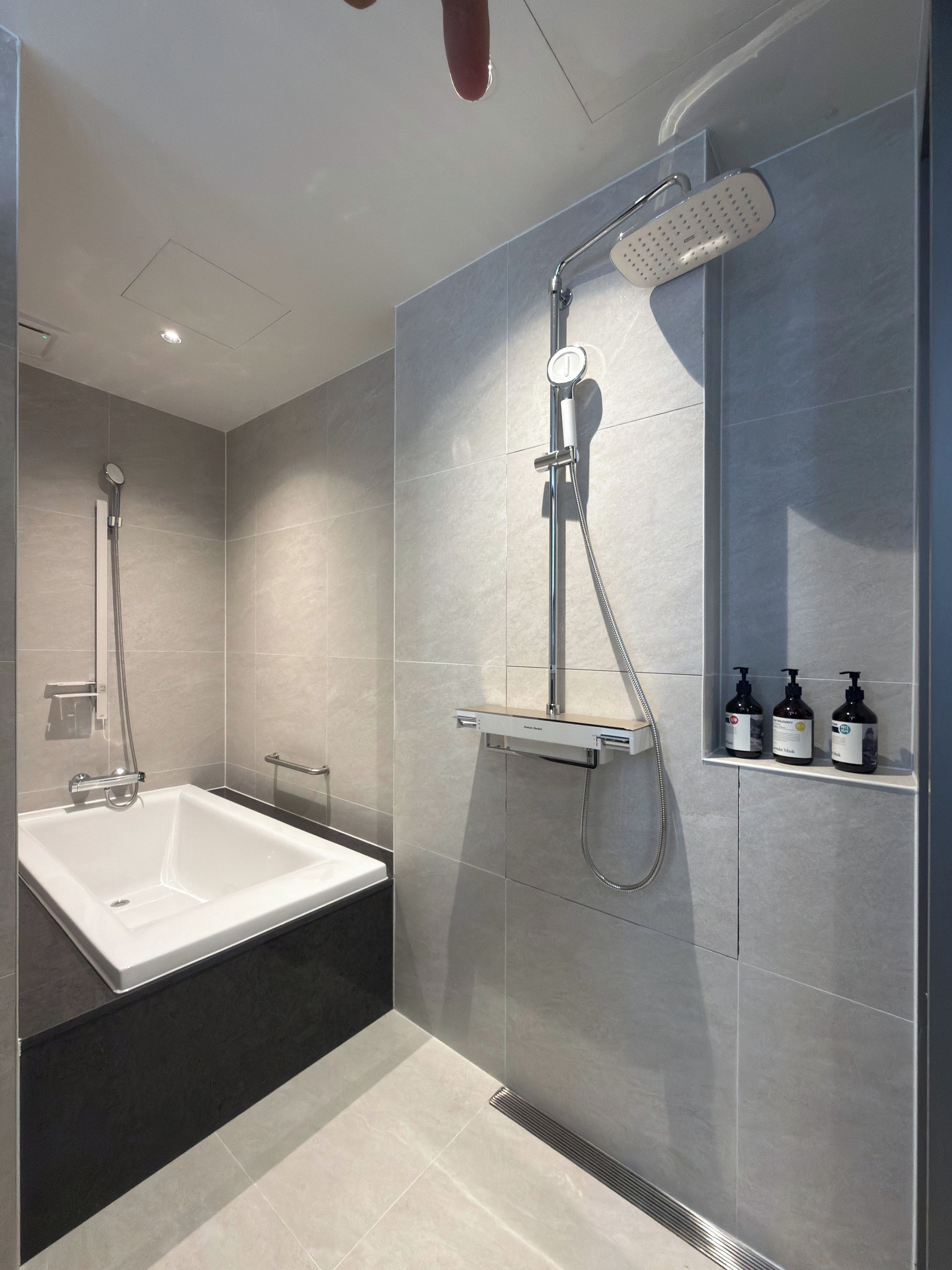 A modern bathroom with a bathtub, a shower with a handheld showerhead, and a shelf with toiletries.