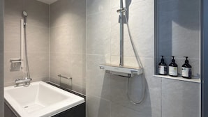 Casa de banho moderna com banheira, chuveiro com duche manual e prateleira com artigos de higiene pessoal.