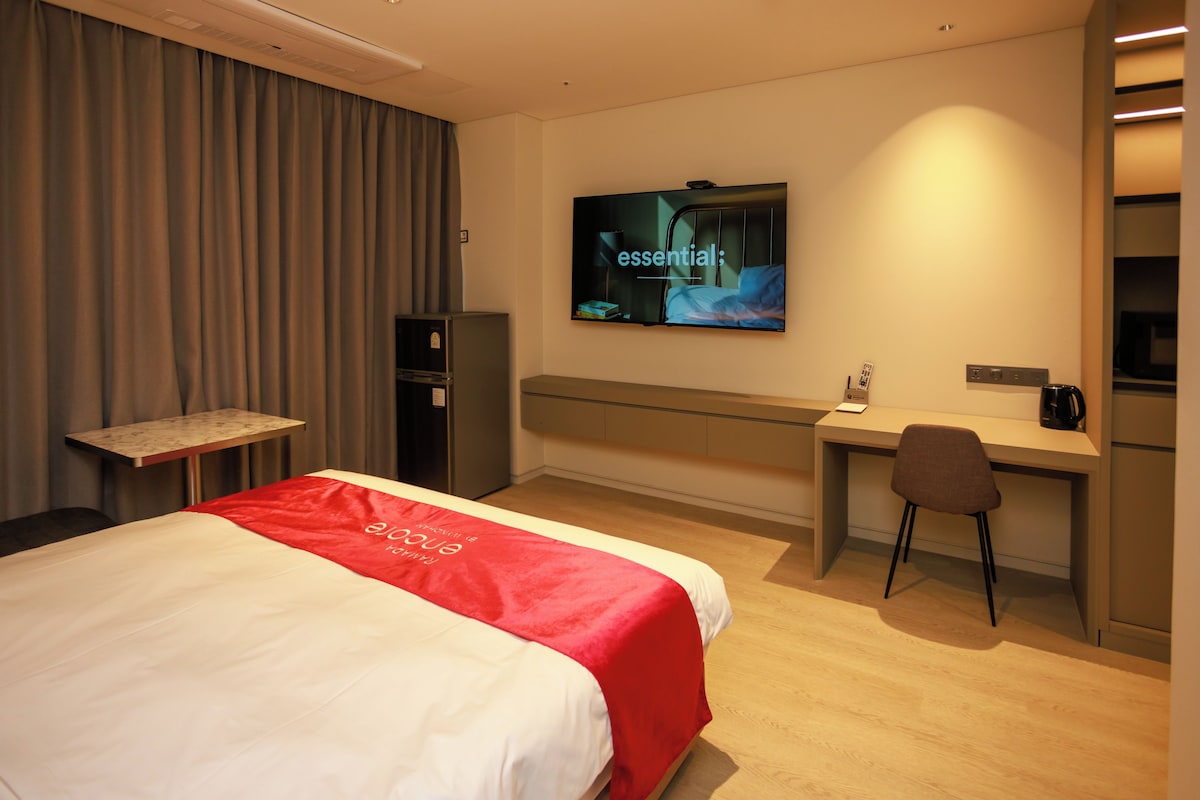 A hotel room with a bed, a desk, a chair, a television, and a minibar.
