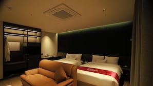 Quarto de hotel com sofá, cama com colcha vermelha, mesa de cabeceira com telefone e espelho.