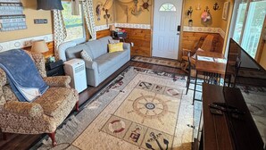L’intérieur chaleureux d’un chalet avec un plafond en bois, une cheminée, un canapé, une table à manger et un tapis orné de motifs marins.