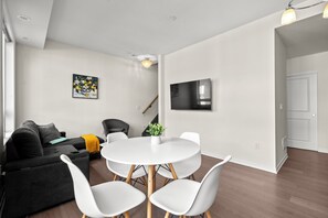 Ein modernes Wohnzimmer mit einem runden Esstisch, weißen Stühlen, einem grauen Sofa und einem flachbildfernseher an der Wand.