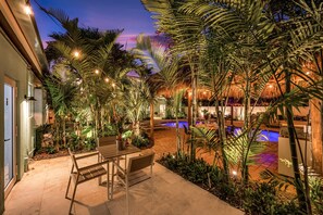 A pool area with a thatched roof, surrounded by palm trees and plants, and a wooden bench. - Walk to Beach / Shared Heated Pool / LostShaker One (Lauderdale-by-the-Sea)