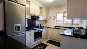 A kitchen with a refrigerator, stove, oven, and a window with blinds. - Central Location |Beach Access  | Patio (Margate)