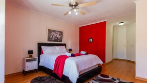 A bedroom with a bed, nightstands, a ceiling fan, a red accent wall, a door, and a patterned rug. - Central Location |Beach Access  | Patio (Margate)