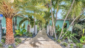 A pathway flanked by palm trees and tropical plants leading to a building with a green facade. - Walk to Beach / Shared Heated Pool / LostShaker Two (Lauderdale-by-the-Sea)