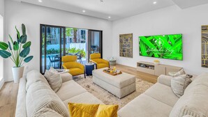 A modern living room with a large TV, comfortable seating, and a view of the outdoors.