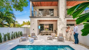 A modern two-story house with a pool, outdoor furniture, and a dining area.
