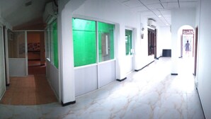 A corridor with tiled flooring, white walls, and green-tinted windows.