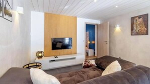 Een moderne woonkamer met een flatscreen televisie, een houten accentmuur, een bank en een bijzettafeltje.