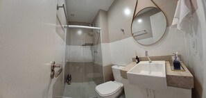 Et moderne badeværelse med et glasafskærmet brusebad, toilet, vask med bordplade og et spejl.